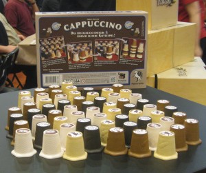 Vor dem Karton des Spiels "Cappucino" stehen die vielen kleinen Becherchen aufgereiht, die man bei diesem Spiel übereinanderstapeln muss.