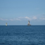 Das Foto zeigt einen kleinen Leuchtturm und eine Boje vor der bretonischen Küste, bei ruhigem Seegang und Sonnenschein.