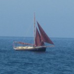 Ein Boot mit von Wind, Sand und Sonne braun gefärbten Segeln auf dem Wasser